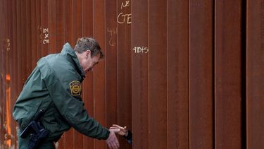 Rodney Scott, jefe del sector de San Diego de la Patrulla Fronteriza, estrechando la mano a otra persona a través de una sección del muro fronterizo, en San Diego.&nbsp;