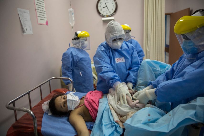 María Álvarez, de 24 años, espera que le entreguen a su bebé recién nacida mientras un obstetra y neonatólogo pinza el cordón umbilical del bebé, en el Instituto Nacional Perinatal en Lima, Perú, el miércoles 29 de julio de 2020.