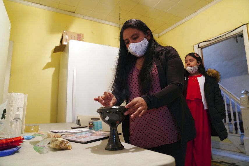 Reyna Mart&iacute;nez enciende un incienso en la cocina de su casa de Queens, Nueva York, antes de iniciar una novena en homenaje a sus padres, fallecidos ambos tras contraer el coronavirus. La acompa&ntilde;a su hija Stephany. Casi un centenar de personas contrajeron el virus en la iglesia a la que iban los padres. Foto del 10 de mayo del 2020.