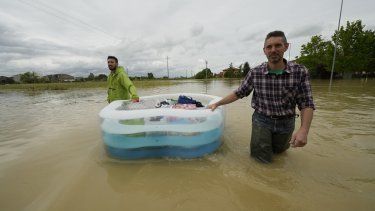 Dos hombres usan una alberca inflable para transportar sus pertenencias en un camino inundado de Lugo, Italia, el jueves 18 de mayo de 2023.&nbsp;