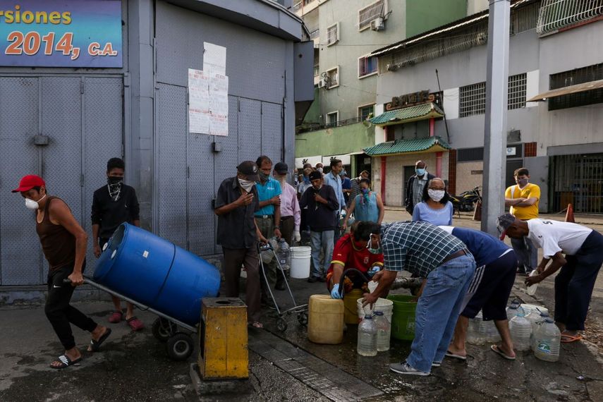 Personas usan mascarillas y pañuelos como medida preventiva contra la pandemia mundial de coronavirus COVID-19, mientras recolectan agua de una tubería&nbsp;en una calle en Caracas, Venezuela, el 21 de marzo de 2020.