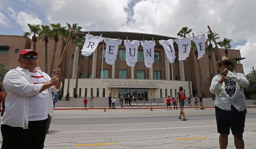 Manifestante sostienen una cuerda con ropa de bebés en la que se lee la palabra reunir durante una protesta contra la política migratoria de tolerancia cero del Gobierno de Trump.