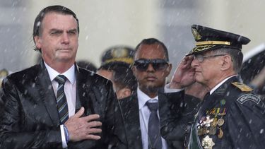 En esta imagen de archivo, el presidente de Brasil, Jair Bolsonaro, se lleva la mano al corazón y el comandante del ejército brasileño Edson Leal Pujol hace un saludo militar durante la interpretación del himno en una ceremonia, celebrada bajo un intenso aguacero, para conmemorar el Día del Ejército, en Brasilia, Brasil. En el inicio de su segundo año como presidente, Bolsonaro se ha mantenido firme en sus combativas políticas mientras se enfrentó a sus críticos tanto dentro como fuera del país.&nbsp;
