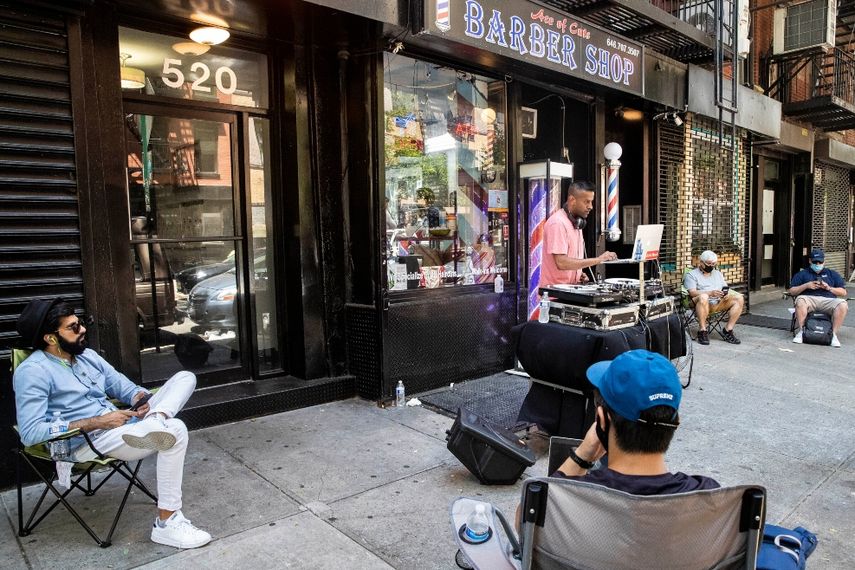Varios clientes aguardan en la acera para que les corten el cabello mientras un DJ toca fuera de la barber&iacute;a Ace of Cuts el lunes 22 de junio de 2020, en Nueva York. Por primera vez en tres meses, los neoyorquinos podr&aacute;n asistir a peluquer&iacute;as y salones de belleza o salir a cenar, aunque solamente en mesas al aire libre.