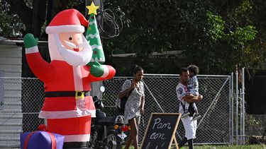 Varias personas pasan junto a un Papá Noel inflable y un cartel que dice Pan y cochinillo. ¡Delicioso! en La Habana, el 23 de diciembre de 2025.&nbsp;