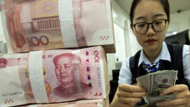 Una empleada de un banco cuenta billetes de dólar junto a fajos de billetes de 100 yuanes, en una sucursal bancaria en Haian, en la provincia de Jiangsu, en el este de China.