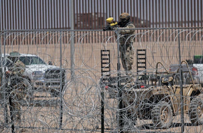 Un miembro de la Guardia Nacional de Texas custodia la frontera con un arma de perdigones de gas mientras centenares de migrantes se manifiestan en el río Grande para pedir autorización para ingresar a Estados Unidos, el 25 de abril de 2024.