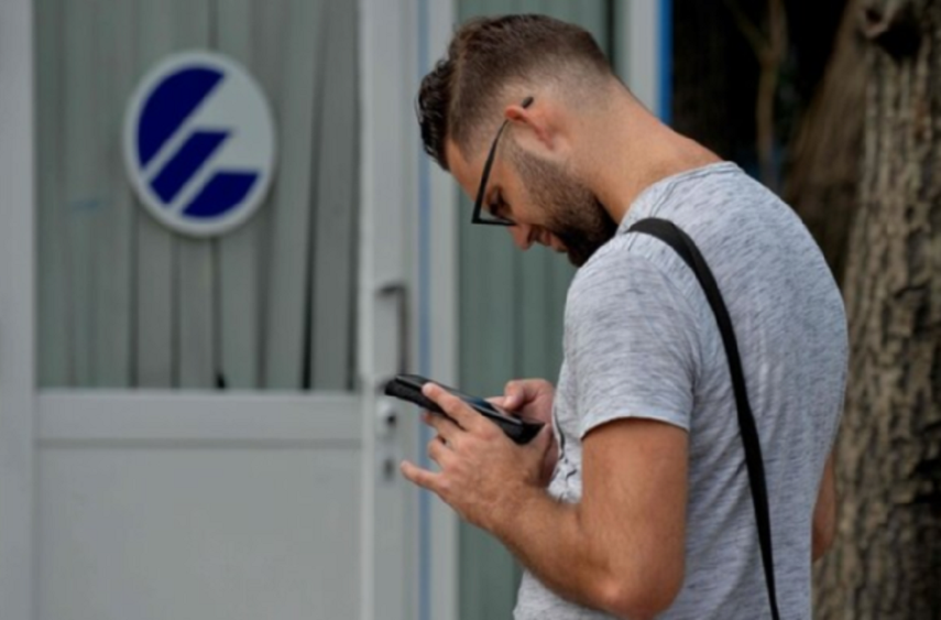 Un joven frente a un cartel de Etecsa en Cuba.