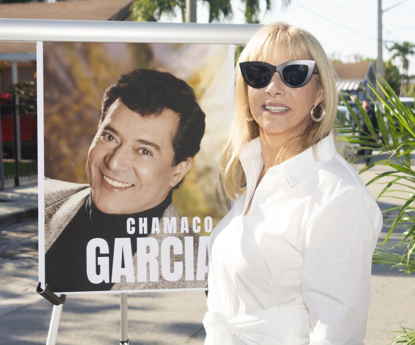 Lucy García posa junto al retrato de Chamaco García, durante la ceremonia de nombramiento de una calle en Miami en honor al artista.&nbsp;