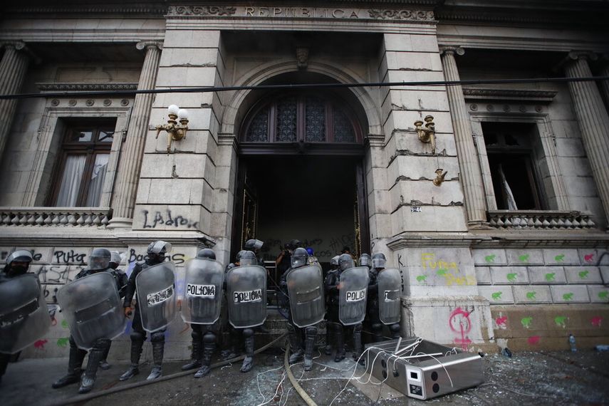 La policía antimotines forma un cordón mientras salen llamas de la sede del Congreso después de que manifestantes incendiaran una parte del edificio, el sábado 21 de noviembre de 2020, en Ciudad de Guatemala.
