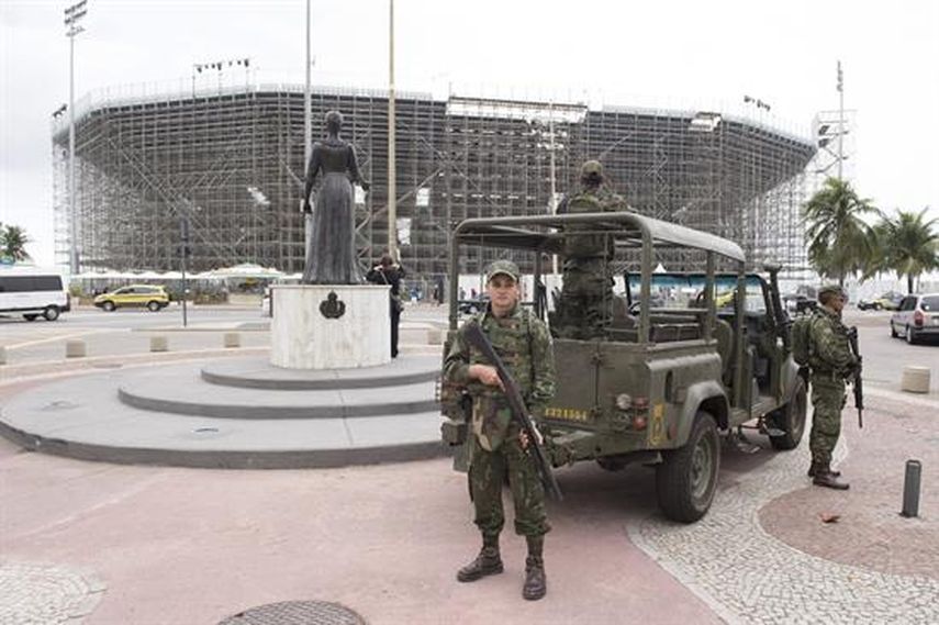 Varios miembros de las fuerzas de seguridad vigilan delante del pabellón, rodeado de andamios, que albergará los partidos de voleibol playa. (EFE)