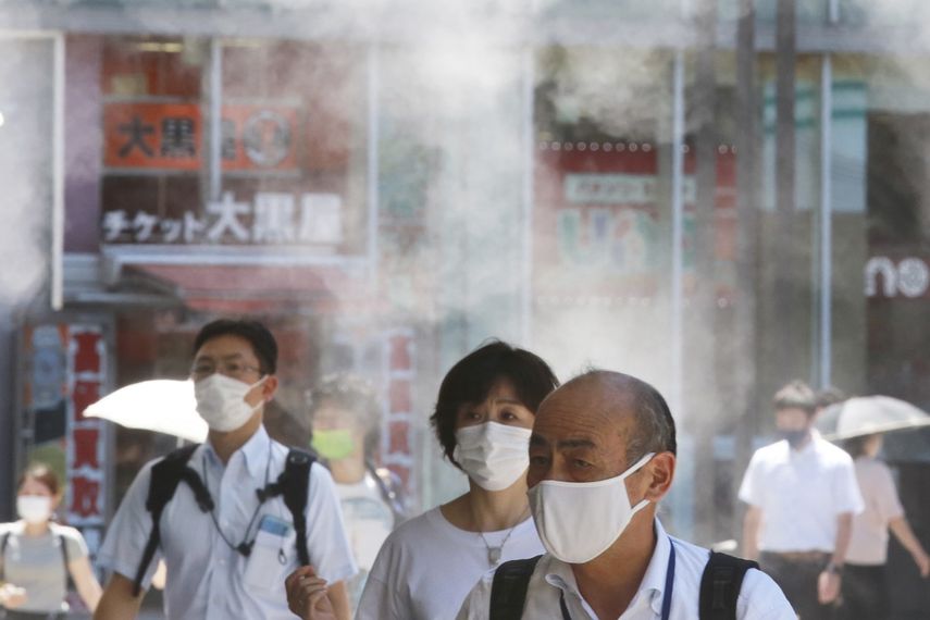 Gente con mascarillas para protegerse contra la expansión del coronavirus caminan bajo agua vaporizada en Tokio, el jueves 5 de agosto de 2021.&nbsp;