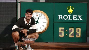 El español Carlos Alcaraz posa el trofeo junto al reloj que marca la duración del partido, el más largo para una final de Roland-Garros, después de ganar al italiano Jannik Sinner al final de su partido final individual masculino en el día 15 del torneo de tenis Roland-Garros en la cancha Philippe-Chatrier en el Complejo Roland-Garros en París el 8 de junio de 2025.