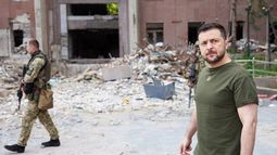 Esta fotografía tomada y publicada por el servicio de prensa de la presidencia ucraniana el 18 de junio de 2022 muestra al presidente ucraniano Volodímir Zelenski (derecha) caminando frente a un edificio parcialmente destruido durante su visita a la posición de las tropas ucranianas en la región de Mykolaiv. &nbsp;
