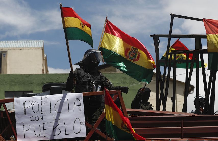 Miembros de la policía agitan banderas bolivianas desde la azotea de una estación policial a pocos metros del palacio presidencial, en La Paz, Bolivia, el sábado 9 de noviembre de 2019. 