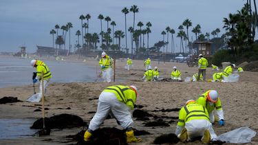 Trabajadores en trajes de protección limpian una playa contaminada de Corona del Mar, en el sur de California, el 7 de octubre de 2021.