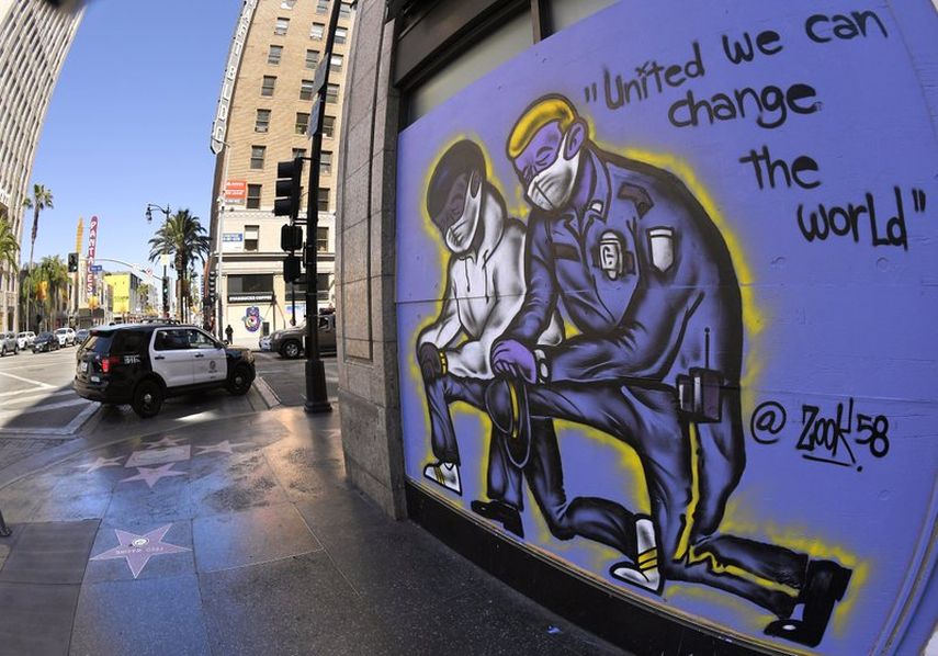 Un mural dibujado en los tablones que protegen un negocio mientras una patrulla del Departamento de Polic&iacute;a de Los &Aacute;ngeles pasa por el lugar, el martes 9 de junio de 2020, en la secci&oacute;n de Hollywood, en Los &Aacute;ngeles.