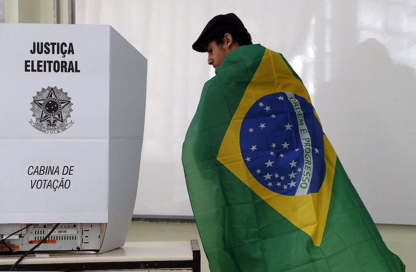Un hombre envuelto en una bandera brasileña se prepara para emitir su voto durante las elecciones legislativas y presidenciales en Sao Paulo, Brasil, el 2 de octubre de 2022.&nbsp; &nbsp;