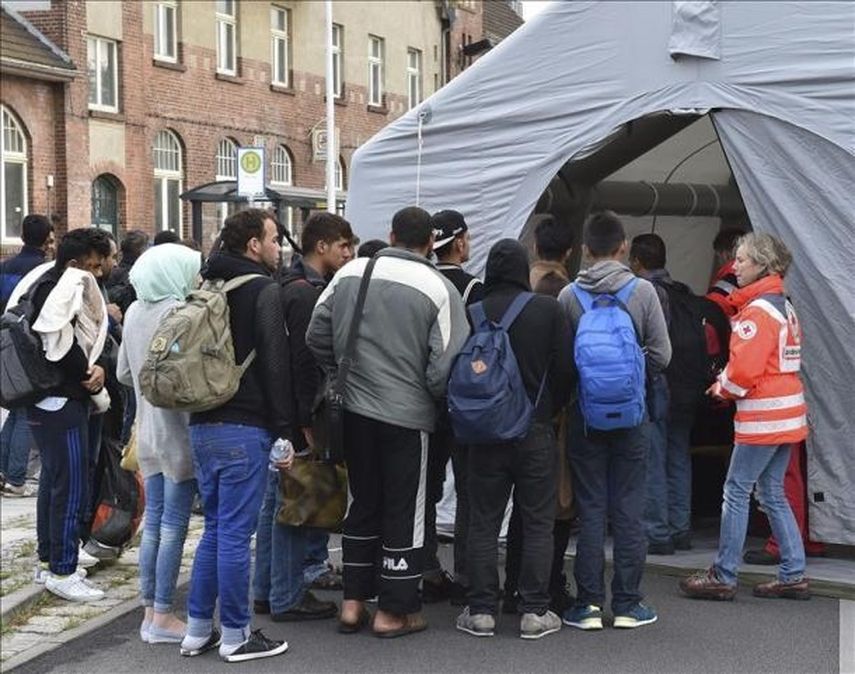Un grupo de refugiados hace cola frente al lugar donde le harán un chequeo médico (EFE)