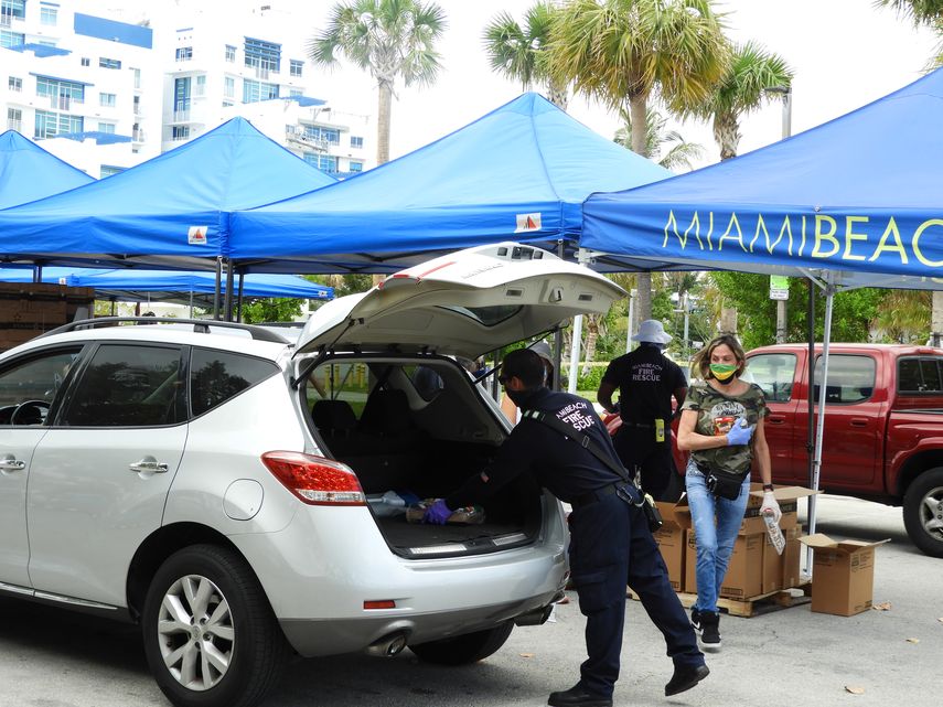 Bomberos y voluntarios de Miami Beach llenan con alimentos el maletero de un auto.