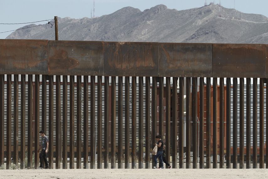 Fotografía del 17 de julio de 2019 de tres migrantes que caminan junto a la valla fronteriza en El Paso, Texas, tras cruzar el río Bravo desde territorio mexicano.