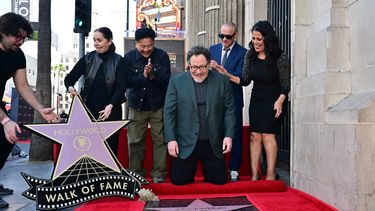 El actor estadounidense Robert Downey Jr. coloca el primer chicle en la recién inaugurada estrella del Paseo de la Fama de Hollywood de John Favreau el 13 de febrero de 2023 en Hollywood, California, mientras Favreau y el chef Roy Choi reaccionan.