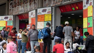 Un grupo de personas hace fila para comprar salchichas y queso en una tienda cerca del mercado municipal de Quinta Crespo que muestra los precios en dólares en Caracas, Venezuela.
