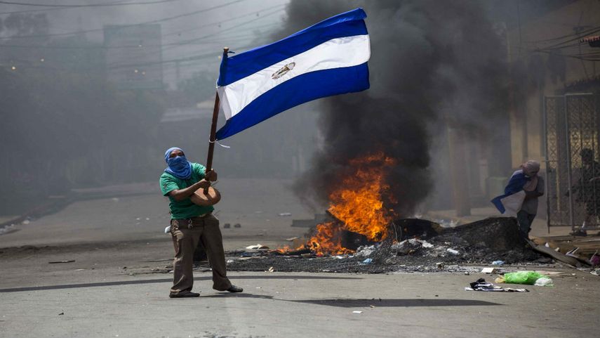 Un joven corre con la bandera de Nicaragua frente a unas llantas incendiadas durante las protestas contra Daniel Ortega.