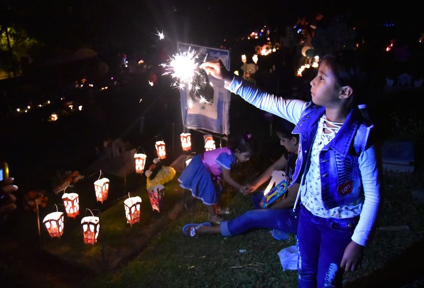 Una niña juega con una velita de pólvora junto a una tumba en un cementerio de Cali.&nbsp;
