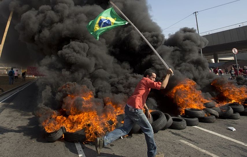 Un integrante del grupo Movimiento de Trabajadores sin Techo porta una bandera brasileña frente a neumáticos quemados en una protesta contra el dinero gastado en el Mundial, en Sao Paulo, cerca del estadio Itaquerao. (AP)