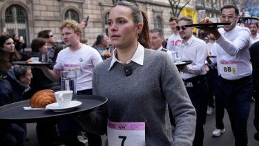 Meseros llevan bandejas con una taza de café, un croissant y un vaso con agua mientras compiten en una carrera de camareros en las calles de París, el domingo 24 de marzo de 2024.&nbsp;