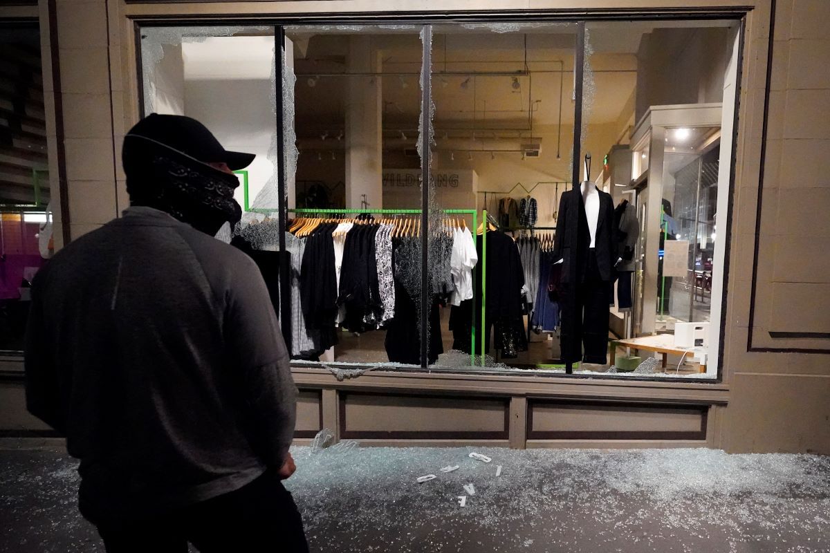 Un hombre permanece frente a un escaparate roto en una tienda durante protestas en Portland, Oregon. Un hombre permanece frente a un escaparate roto en una tienda durante protestas en Portland, Oregon.