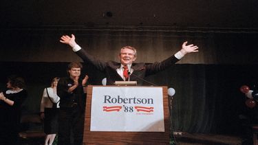 El aspirante a presidente republicano Pat Robertson levanta los brazos el 8 de marzo de 1988 en respuesta a los vítores de sus seguidores, mientras el cantante de country Ricky Skaggs aplaude en un mitin de campaña en Spartanburg, EEUU.