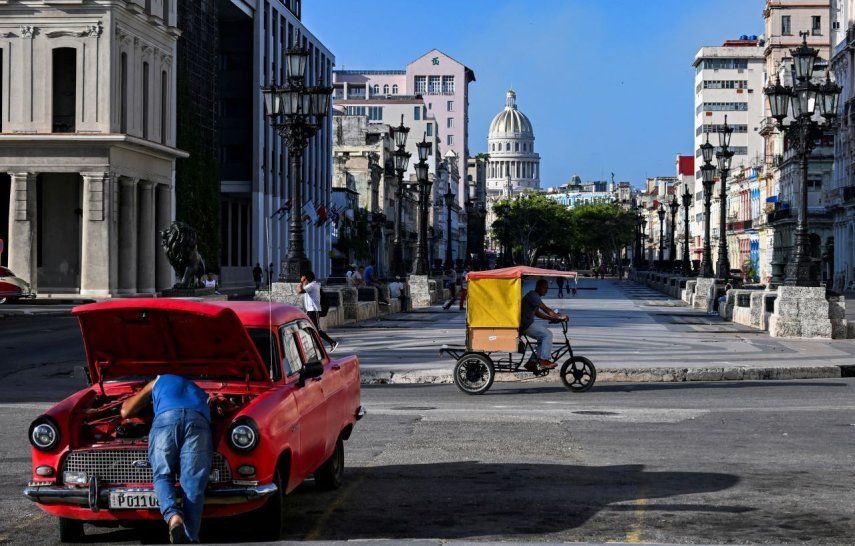 Un hombre repara su antiguo carro en medio de la calle, mientras un hombre en su bicitaxi busca clientes a quienes llevar en una de las calles de La Habana, Cuba.