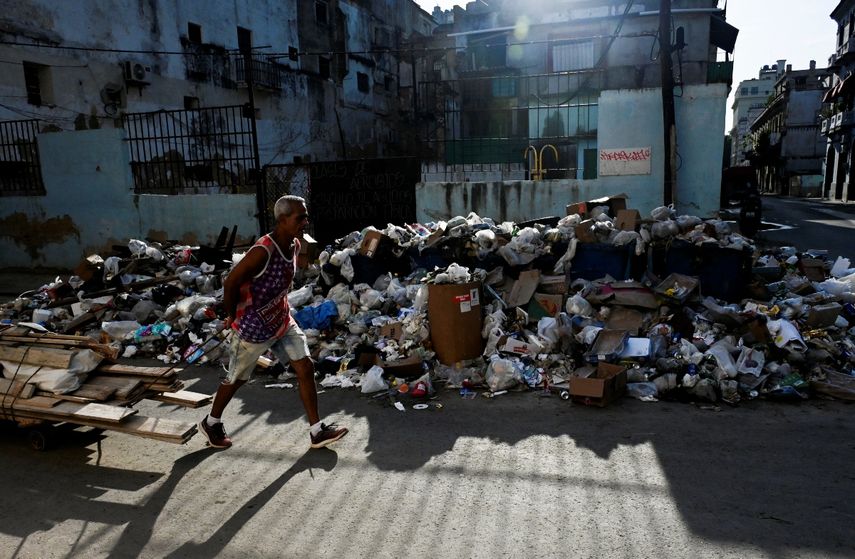 Un hombre transporta trozos de madera cerca de una gran cantidad de basura en una calle de La Habana el 21 de agosto de 2024. La Habana acumula más de 30.000 metros cúbicos de basura diarios, siete mil más que hace un año, según cifras oficiales.