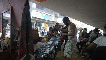 Reflejado en un espejo, Alejandro Palencia le corta el pelo a un niño el jueves 12 de agosto de 2021 en su peluquería debajo de un puente, en el centro de Caracas, Venezuela.&nbsp;