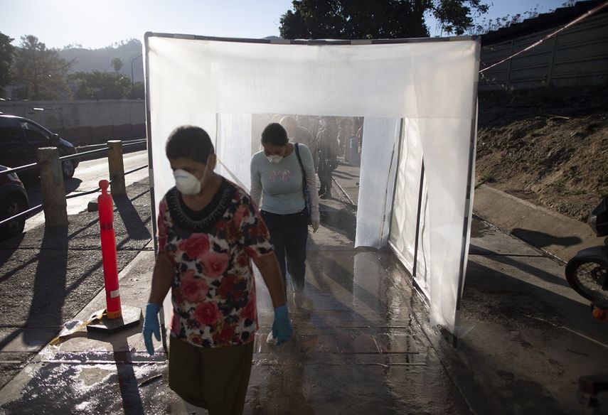 En esta fotografía de archivo del 18 de marzo de 2020, personas con mascarillas protectoras y guantes plásticos caminan por una cámara de descontaminación. Muchos venezolanos se resisten a hacerse la prueba del nuevo coronavirus por temor a ser encerrados en centros obligatorios de aislamiento si se descubre que están infectados. 