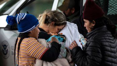 Una solicitante de asilo nicaragüense (izquierda) carga a su sobrino de dos meses antes de dárselo a su madre (derecha) mientras una solicitante de asilo cubana besa a su hijo de cuatro años mientras esperan que un agente de la Patrulla Fronteriza tome su información, en Eagle Pass, Texas el 19 de diciembre de 2022.