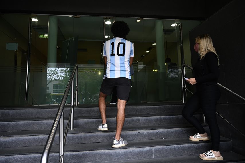 Un joven con la camiseta del dorsal 10, que usó Maradona, posa frente a la clínica en la que está internado el astro del balompié