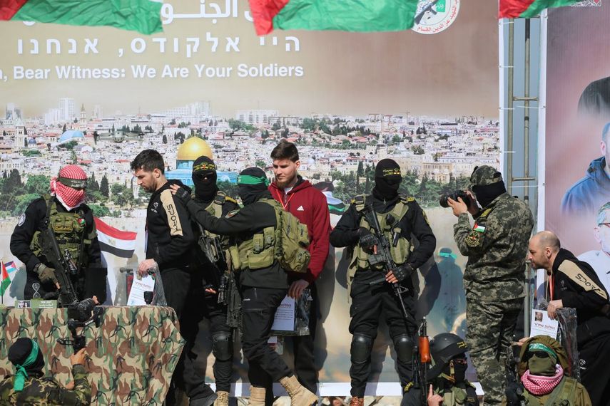 El rehén israelí-ruso Sasha Trupanov (C) observa cómo el israelí-estadounidense Sagui Dekel-Chen (2º izq.) y el israelí-argentino Yair Horn (der.) que suben al escenario, bajo la atenta mirada de comandos terroristas fuertemente armados, durante su entrega a un equipo de la Cruz Roja en Khan Yunis, en el sur de la Franja de Gaza, el 15 de febrero de 2025, como parte del sexto intercambio de rehenes y prisioneros.