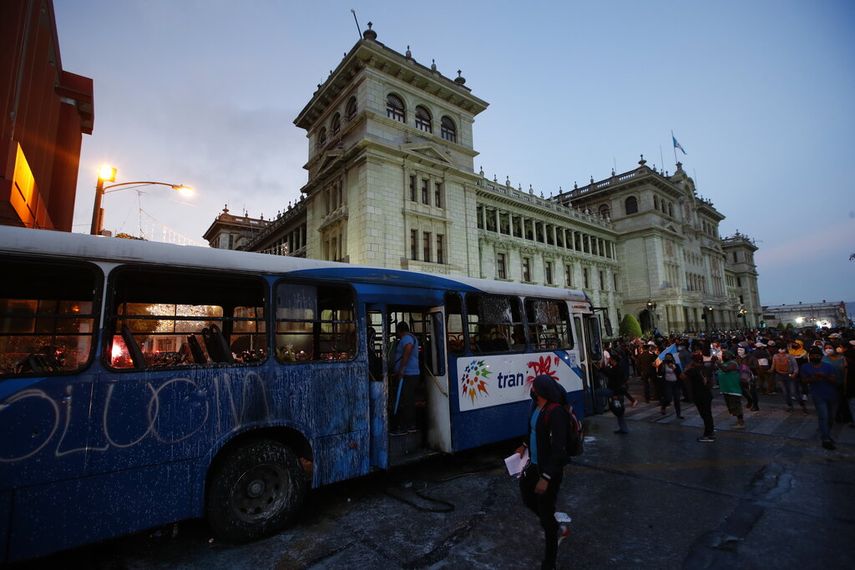 Manifestantes se acercan a un autobús dañado por manifestantes frente al Palacio Nacional para exigir la renuncia del presidente Alejandro Giammattei, en la Ciudad de Guatemala, el sábado 28 de noviembre de 2020.