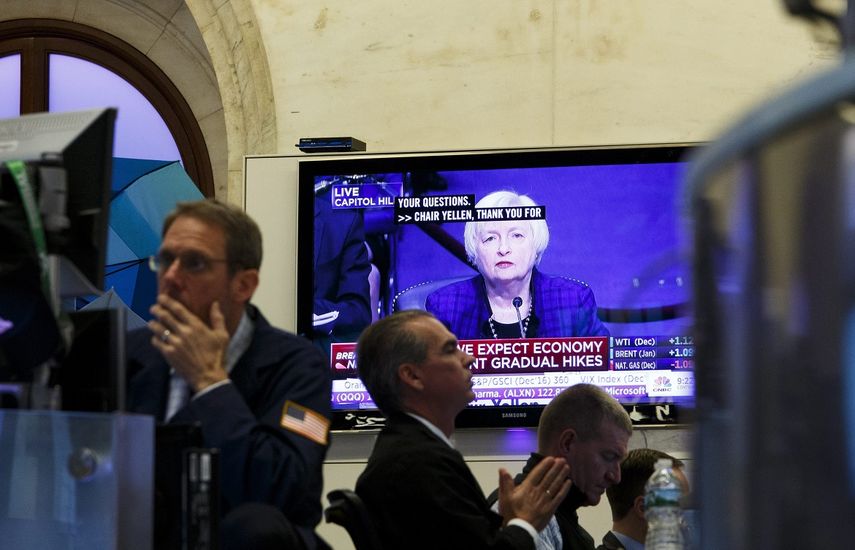 Una pantalla muestra una imagen de la presidenta de la Reserva Federal estadounidense,&nbsp;Janet&nbsp;Yellen, mientras varios agentes de Bolsa realizan su trabajo en el parqué de Nueva York