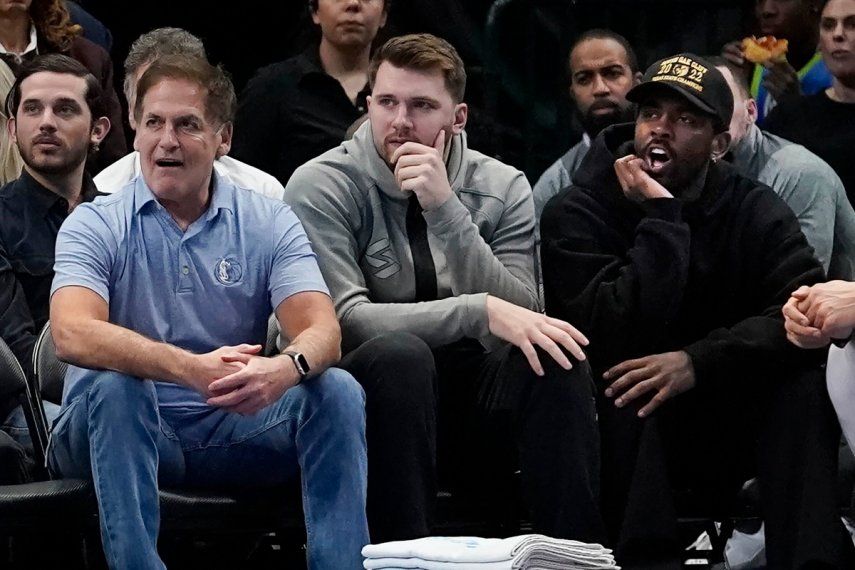Mark Cuban (izquierda), dueño de los Mavericks de Dallas, aparece sentado junto a los jugadores Luka Doncic (centro) y Kyrie Irving durante el juego ante los Grizzlies de Memphis, el 13 de marzo de 2023.