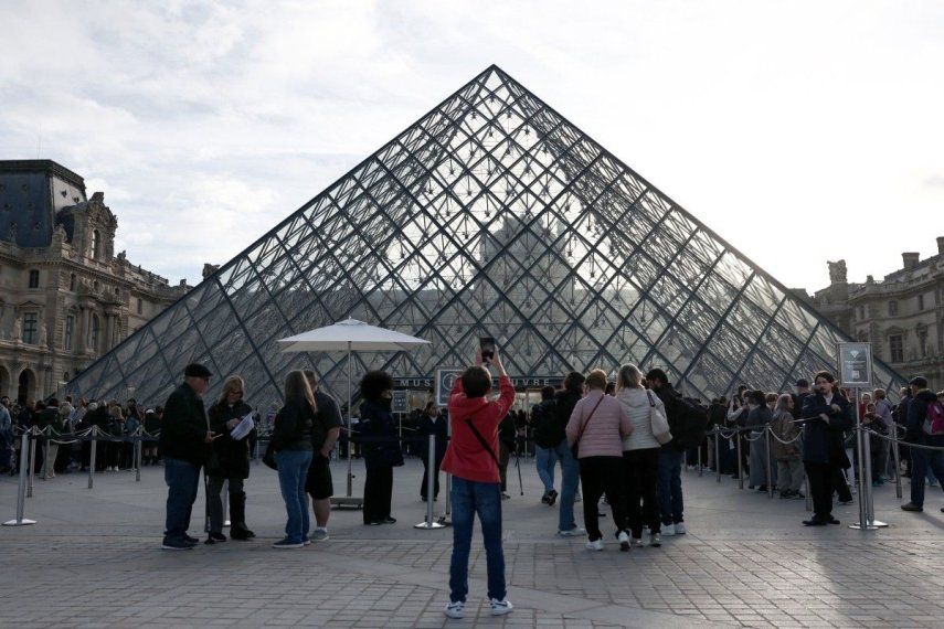 Un peatón toma una fotografía de la Pirámide del Louvre, diseñada por el arquitecto chino-estadounidense Ieoh Ming Pei, con el Museo del Louvre al fondo, mientras los visitantes hacen fila para ingresar, en París, el 22 de octubre de 2025.