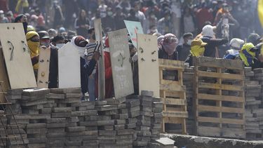 Manifestantes contrarios al gobierno se cubren tras una barricada en choques con la polic&iacute;a en Quito, Ecuador el 12 de octubre de 2019.