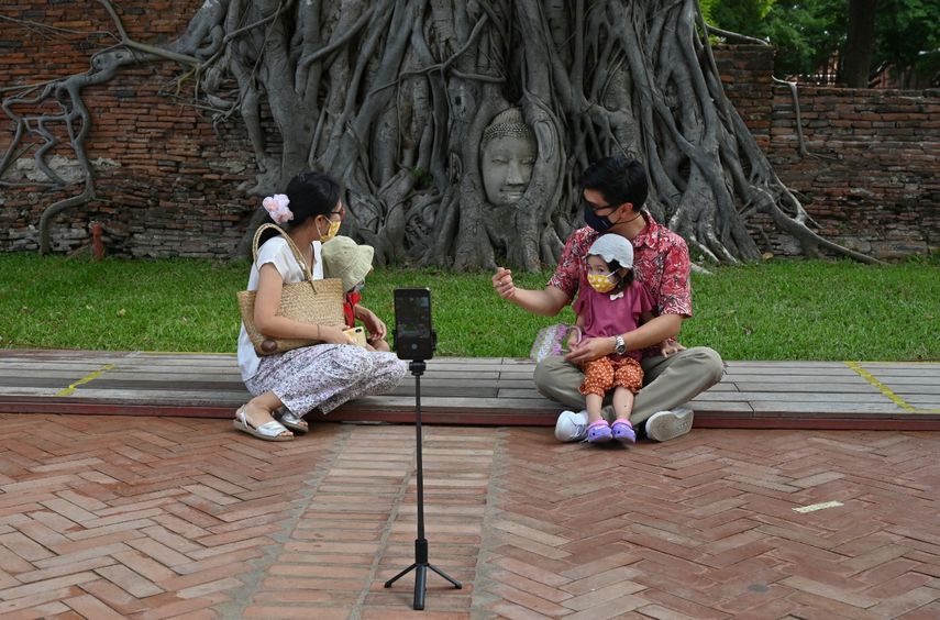 En esta foto tomada el 31 de julio de 2020, una pareja tailandesa y sus hijos posan frente a la cabeza de piedra de Buda cubierta de ra&iacute;ces de &aacute;rboles en el complejo del templo Wat Mahathat del siglo XIV en la antigua capital de Ayutthaya, al norte de Bangkok, cuando las autoridades reabrieron los sitios. a los turistas que siguen bloqueos para detener la propagaci&oacute;n del coronavirus COVID-19.