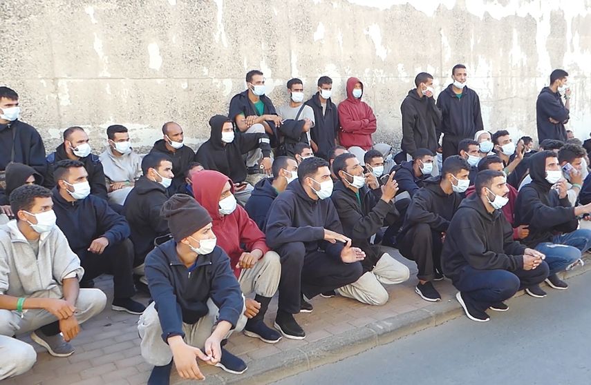 Migrantes marroquíes aguardan por un autobús para ser trasladados a un hotel campamento.