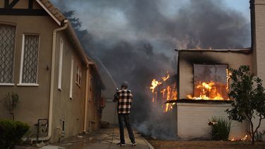 Una persona usa una manguera de jardín para intentar evitar que una casa vecina se incendie durante el incendio de Eaton el 8 de enero de 2025 en Altadena, California.