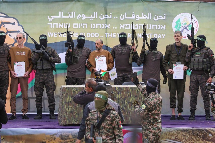 Miembros del grupo terrorista Hamás escoltan a los rehenes israelíes (de izquierda a derecha, con certificados) Ohad Ben Ami, Eli Sharabi y Or Levy en un escenario antes de entregarlos a un equipo de la Cruz Roja en Deir el-Balah, Gaza central, el 8 de febrero de 2025. Militantes de Hamás entregaron a tres rehenes israelíes el 8 de febrero, como parte del quinto intercambio bajo un frágil alto el fuego en Gaza, y 183 prisioneros retenidos por Israel serán liberados más tarde ese mismo día.&nbsp;