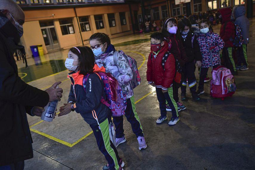 Un grupo de alumnos con mascarilla para prevenir contagios de coronavirus se desinfectan las manos mientras esperan en fila para entrar en la escuela Luis Amigo tras las vacaciones de Navidad, en Pamplona, en el norte de España, el lunes 10 de enero de 2021.&nbsp;